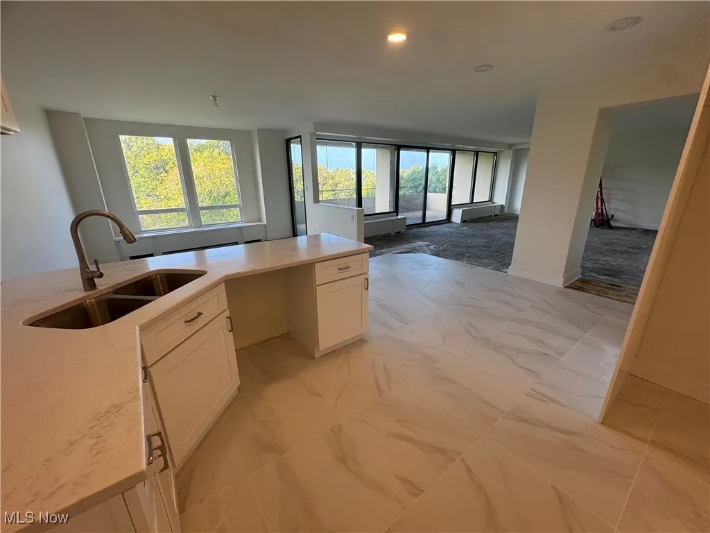 Kitchen with white cabinetry, light stone counters, recessed lighting, open floor plan, and light marble finish floors