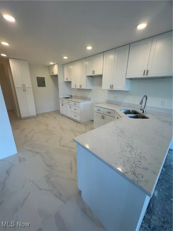 Kitchen featuring light marble finish floors, a peninsula, white cabinetry, recessed lighting, and light stone counters