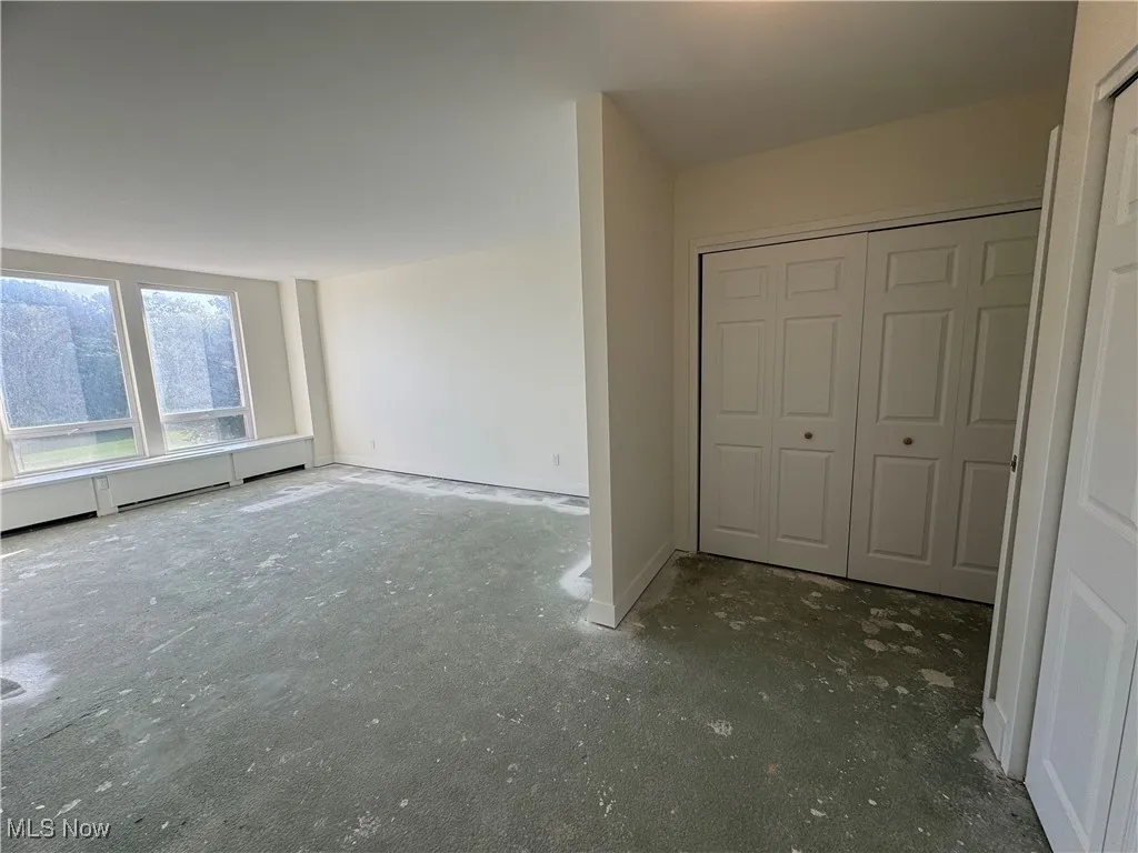Unfurnished bedroom featuring a closet, a baseboard heating unit, and unfinished concrete floors