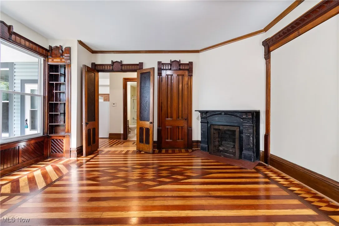 Unfurnished living room featuring inlaid floor details, crown molding, a fireplace with flush hearth, and hardwood / wood-style flooring