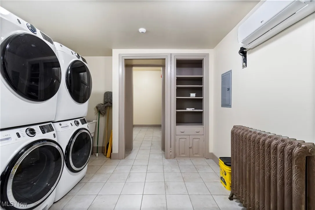 Washroom with an AC wall unit, light tile patterned floors, electric panel, and estacked washer and dryer