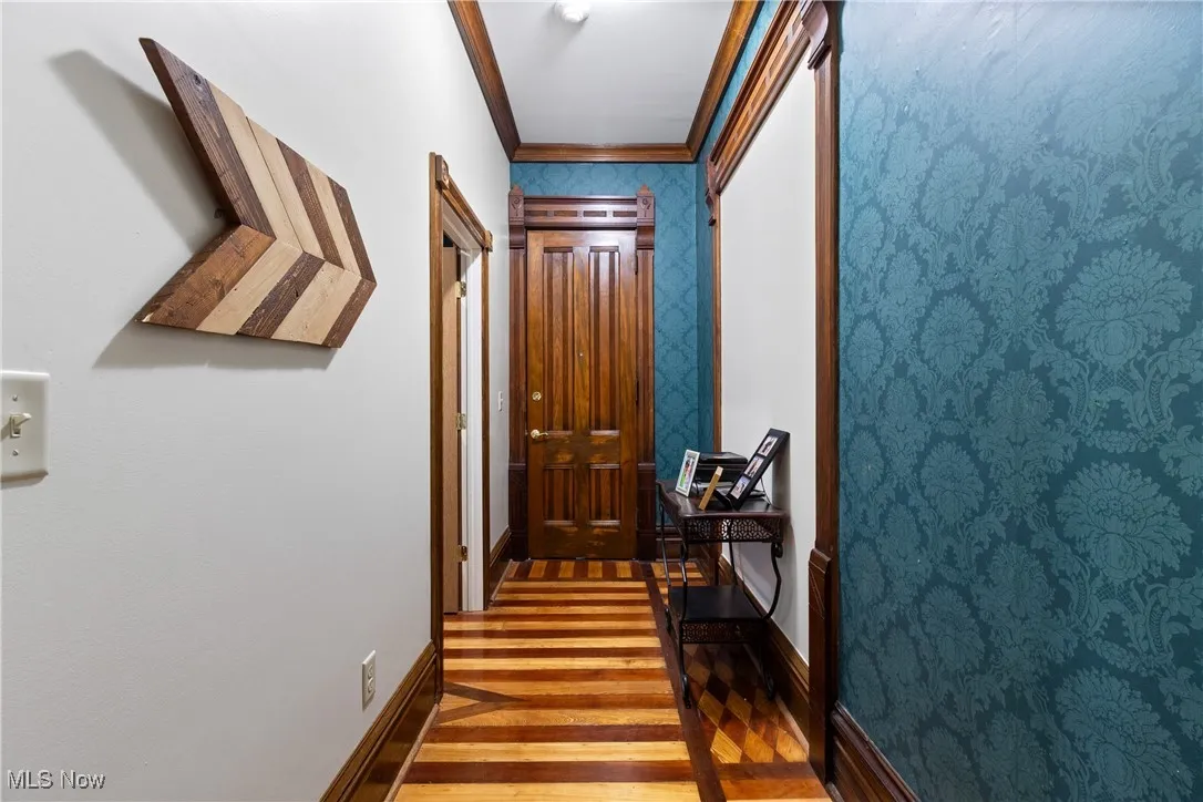 Corridor featuring crown molding, light wood finished floors, and wallpapered walls