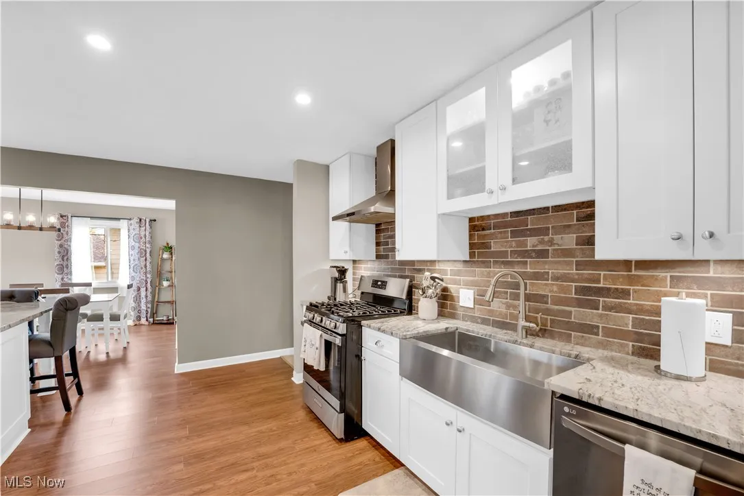Kitchen featuring light stone counters, stainless steel appliances, white cabinetry, decorative backsplash, and wall chimney exhaust hood