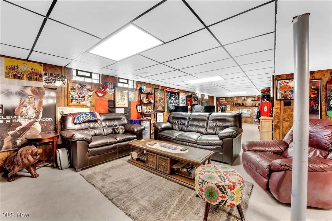 Living room featuring a drop ceiling, wooden walls, and finished concrete flooring