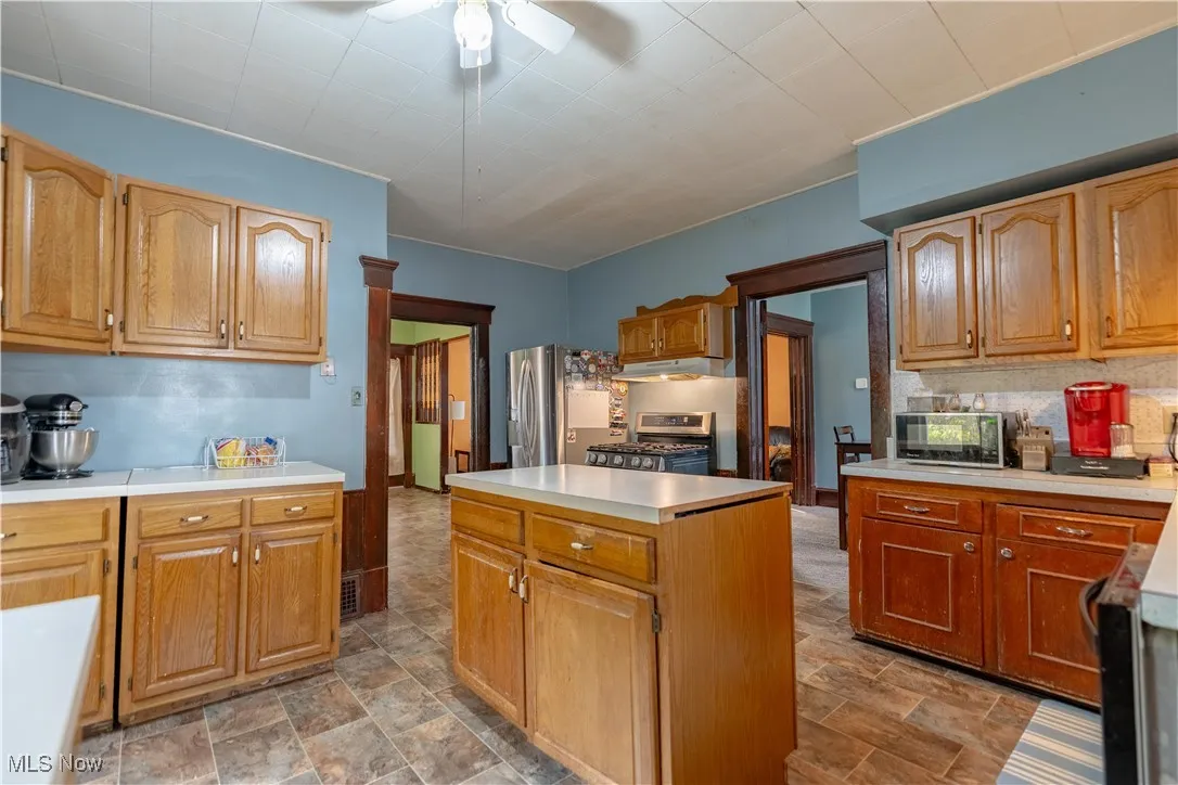 Kitchen featuring light countertops, appliances with stainless steel finishes, decorative backsplash, a center island, and ceiling fan