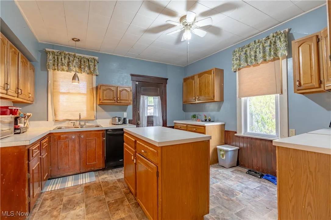 Kitchen featuring wooden walls, a wainscoted wall, light countertops, a center island, and brown cabinetry