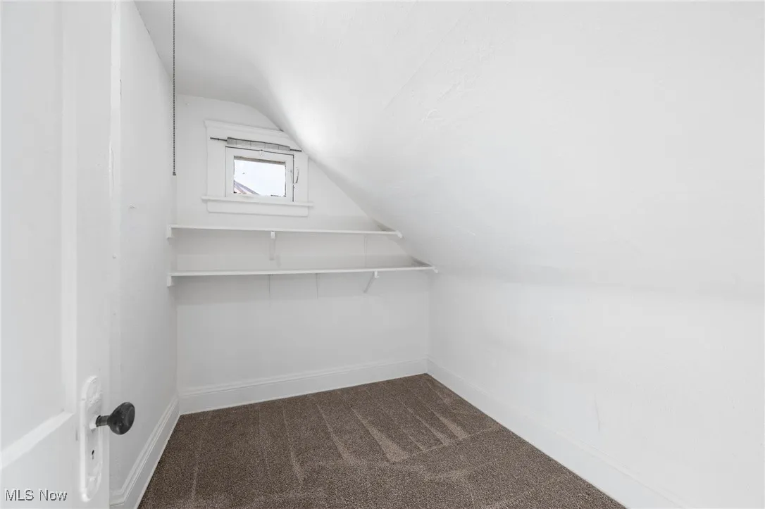Walk in closet with dark colored carpet and vaulted ceiling