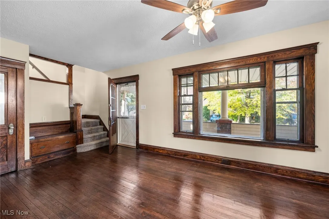 Empty room with dark wood finished floors, a textured ceiling, a ceiling fan, and stairway