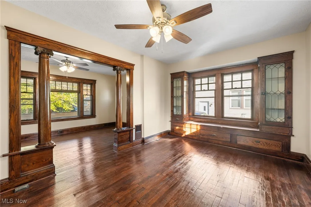 Unfurnished room featuring wood-type flooring, ornate columns, a ceiling fan, and a textured ceiling