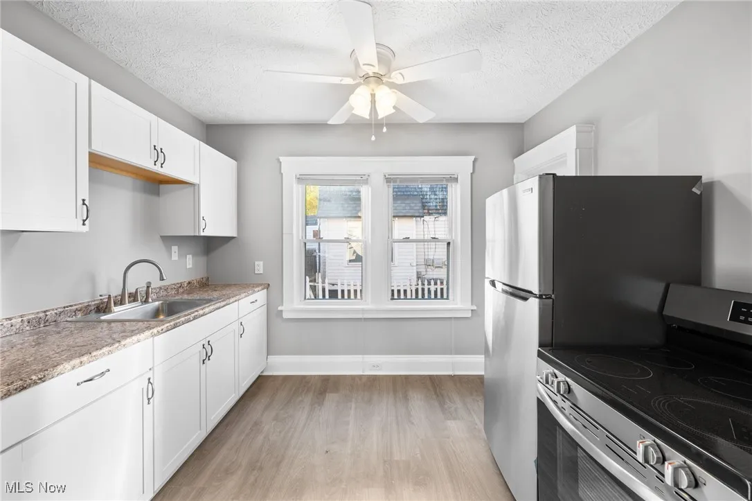 Kitchen with stainless steel electric range oven, light wood finished floors, a textured ceiling, white cabinetry, and ceiling fan