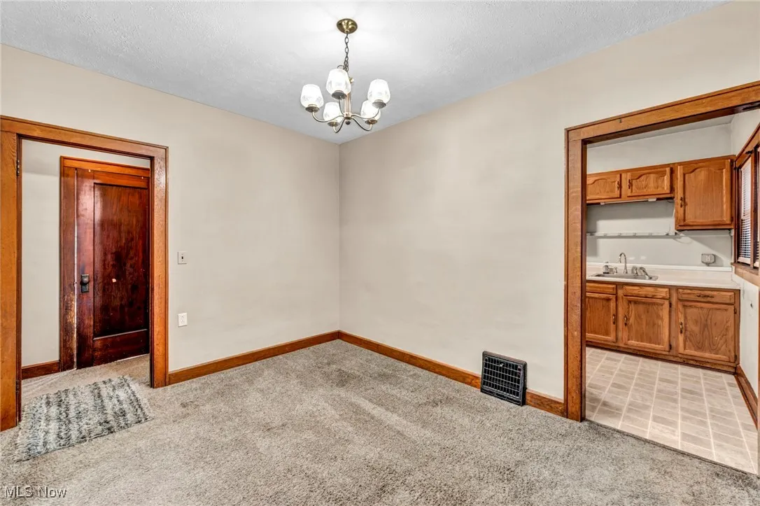 Unfurnished dining area with light colored carpet, a textured ceiling, and a chandelier