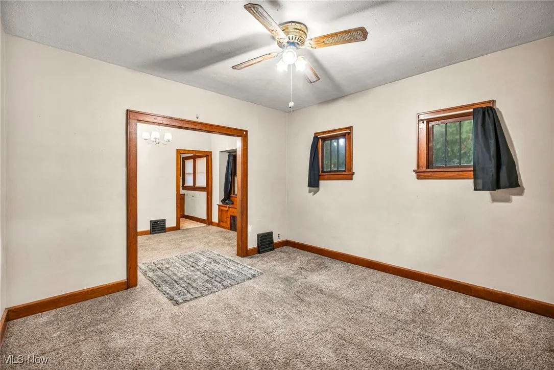 Carpeted empty room featuring a textured ceiling, a chandelier, and ceiling fan