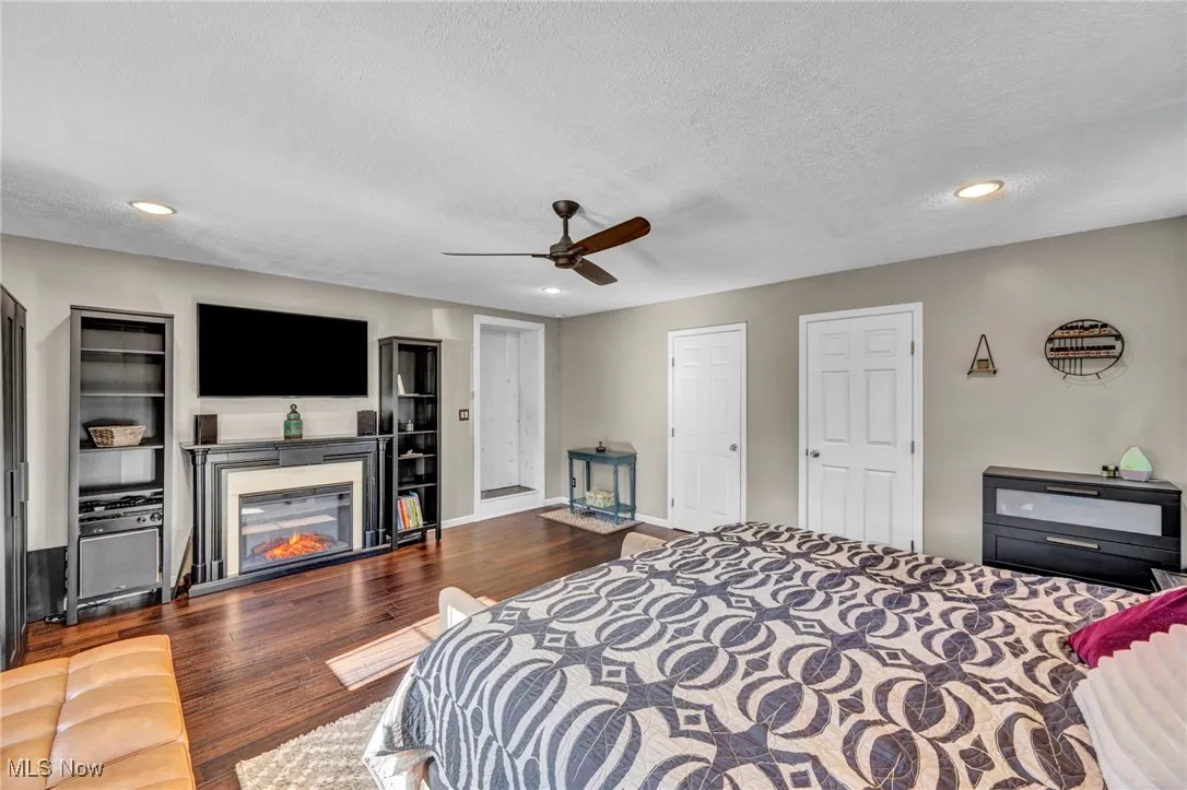 Bedroom with recessed lighting, dark wood-style floors, a textured ceiling, a glass covered fireplace, and a ceiling fan