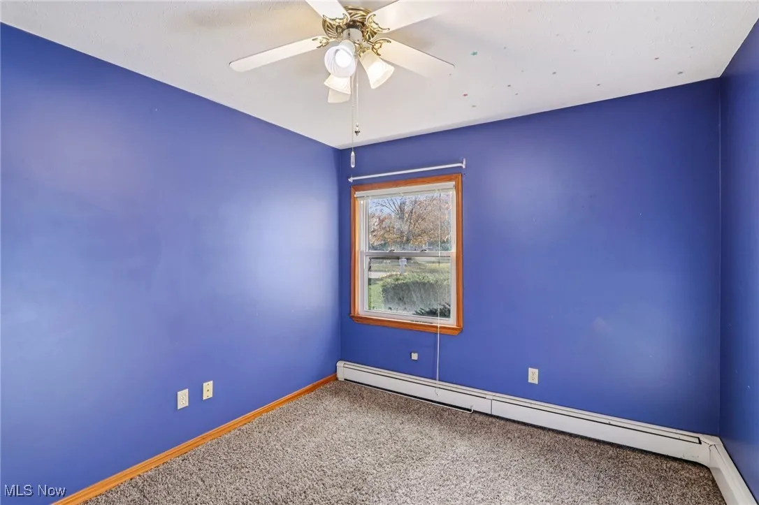 Unfurnished room featuring a baseboard radiator, carpet flooring, and a ceiling fan