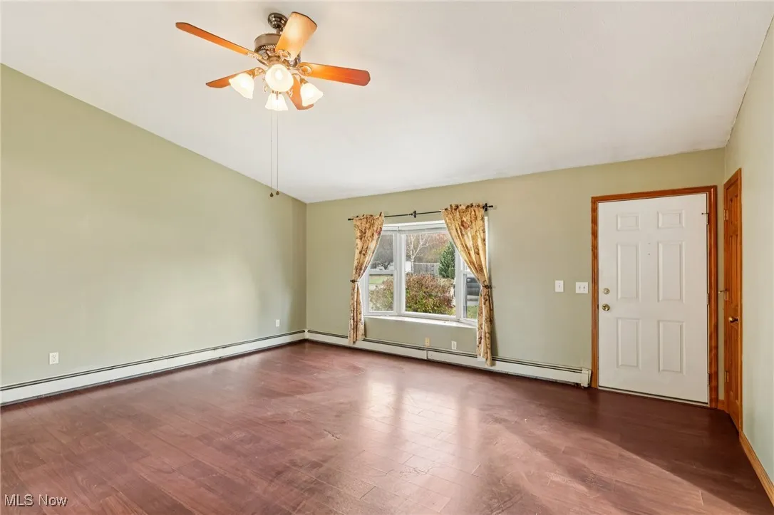 Unfurnished room featuring wood finished floors, a baseboard heating unit, and a ceiling fan