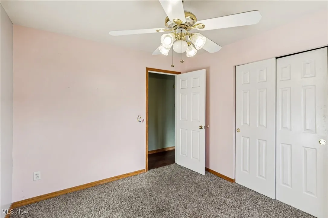 Unfurnished bedroom with dark carpet, a closet, and a ceiling fan