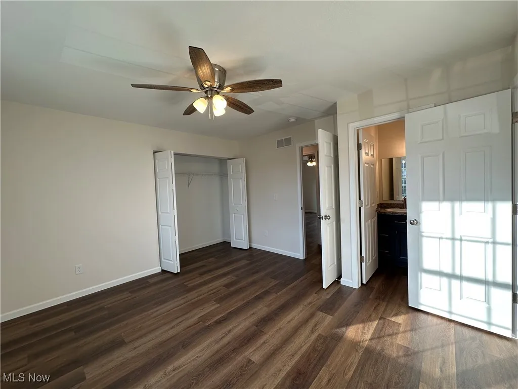 Unfurnished bedroom with dark wood-style flooring, ceiling fan, a closet, and ensuite bath