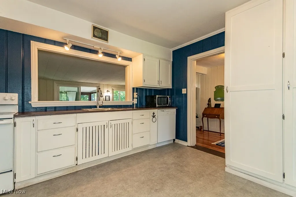 Kitchen featuring dark countertops, white appliances, and white cabinetry