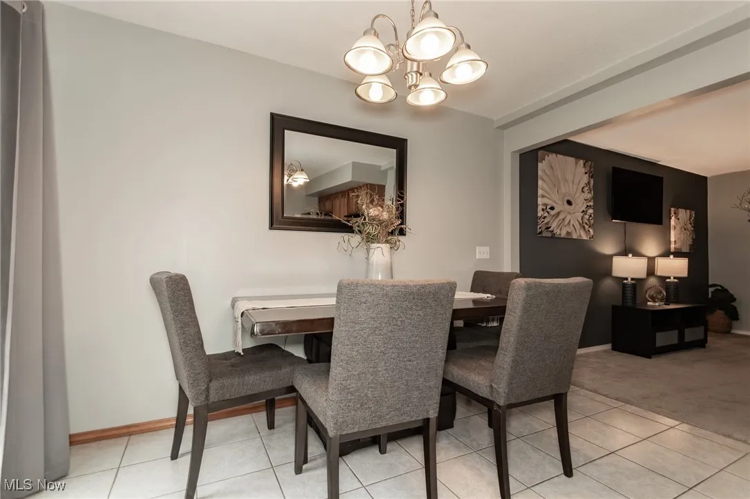 Dining space with light tile patterned floors, a chandelier, and light colored carpet
