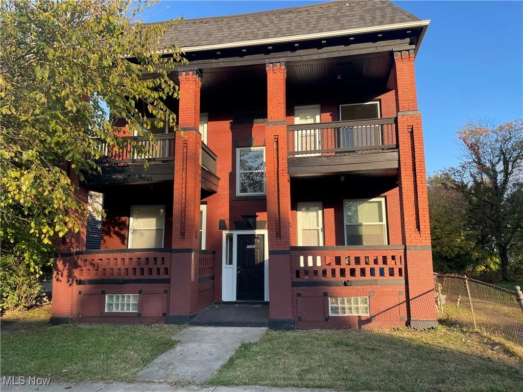View of front of Building featuring brick siding, a balcony, and a shingled roof