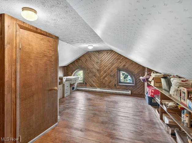 Additional living space featuring wood walls, hardwood / wood-style flooring, a textured ceiling, lofted ceiling, and a baseboard heating unit