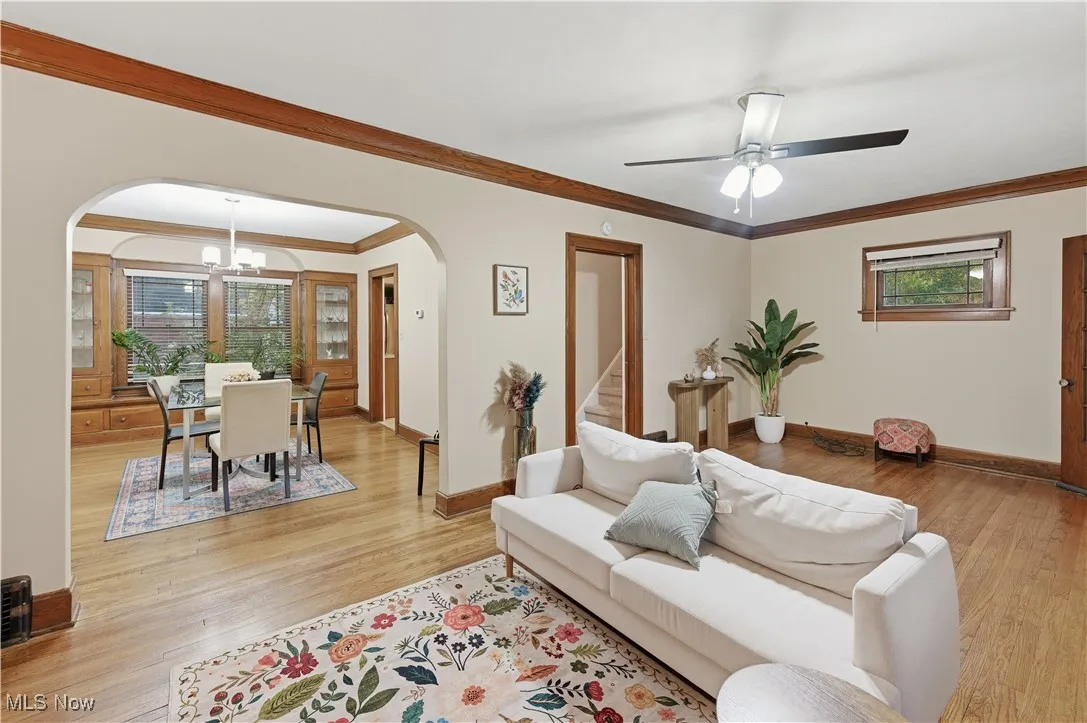 Living room featuring a chandelier, ornamental molding, light wood-type flooring, stairway, and ceiling fan