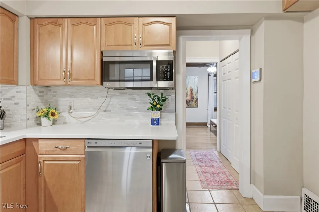 Kitchen featuring stainless steel appliances, light tile patterned floors, tasteful backsplash, and light brown cabinetry