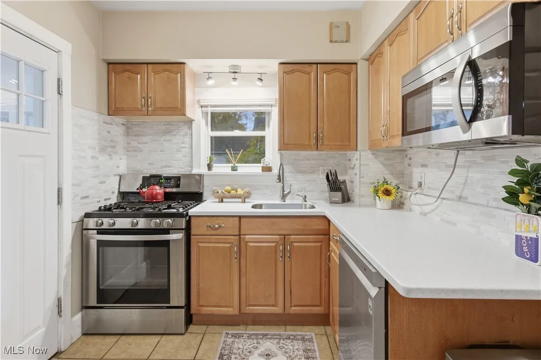 Kitchen with stainless steel appliances, backsplash, light countertops, light tile patterned flooring, and brown cabinetry