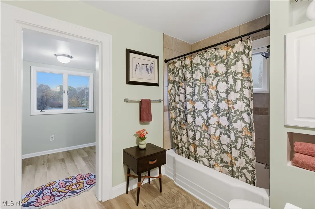 Full bath with shower / tub combo and light wood-style flooring