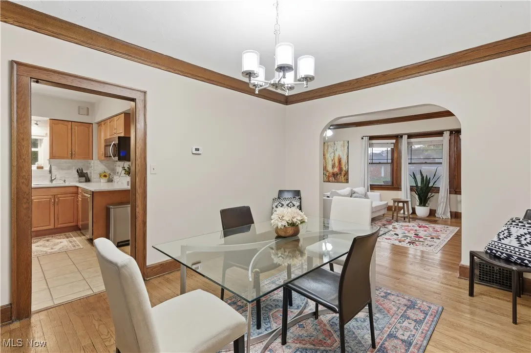 Dining space with crown molding, arched walkways, a chandelier, and light wood-style floors