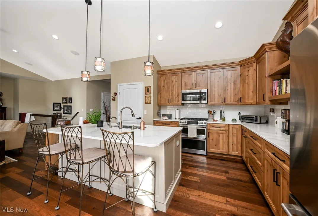 Kitchen with a kitchen bar, decorative backsplash, brown cabinetry, decorative light fixtures, and recessed lighting