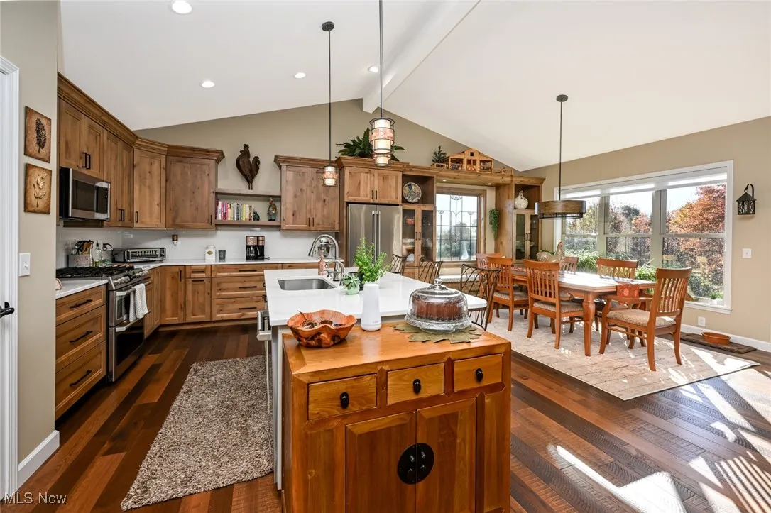 Kitchen featuring brown cabinetry, decorative light fixtures, dark wood-type flooring, and stainless steel appliances