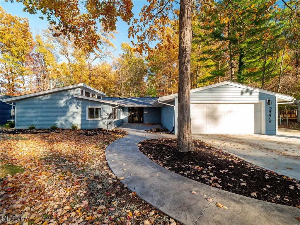 Mid-century inspired home with driveway, a garage, and view of wooded area