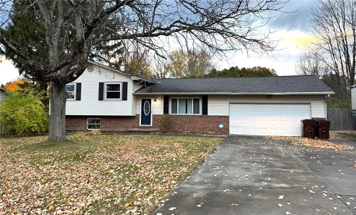 Split level home featuring asphalt driveway, brick siding, an attached garage, and a front lawn