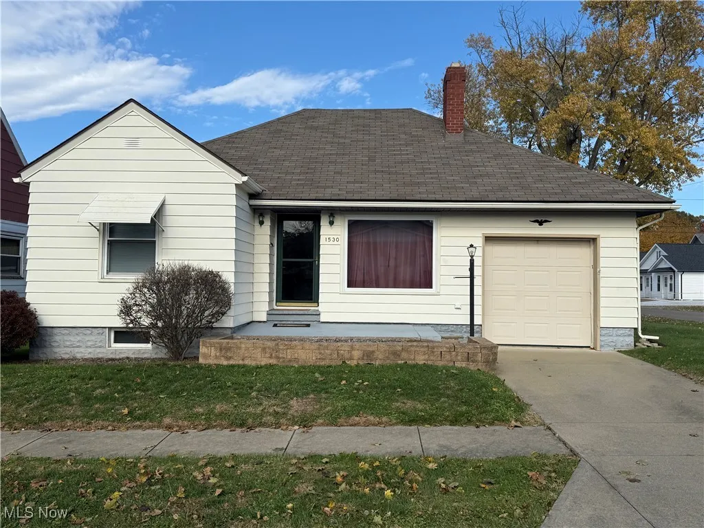 View of front of house featuring a chimney, an attached garage, roof with shingles, and a front yard