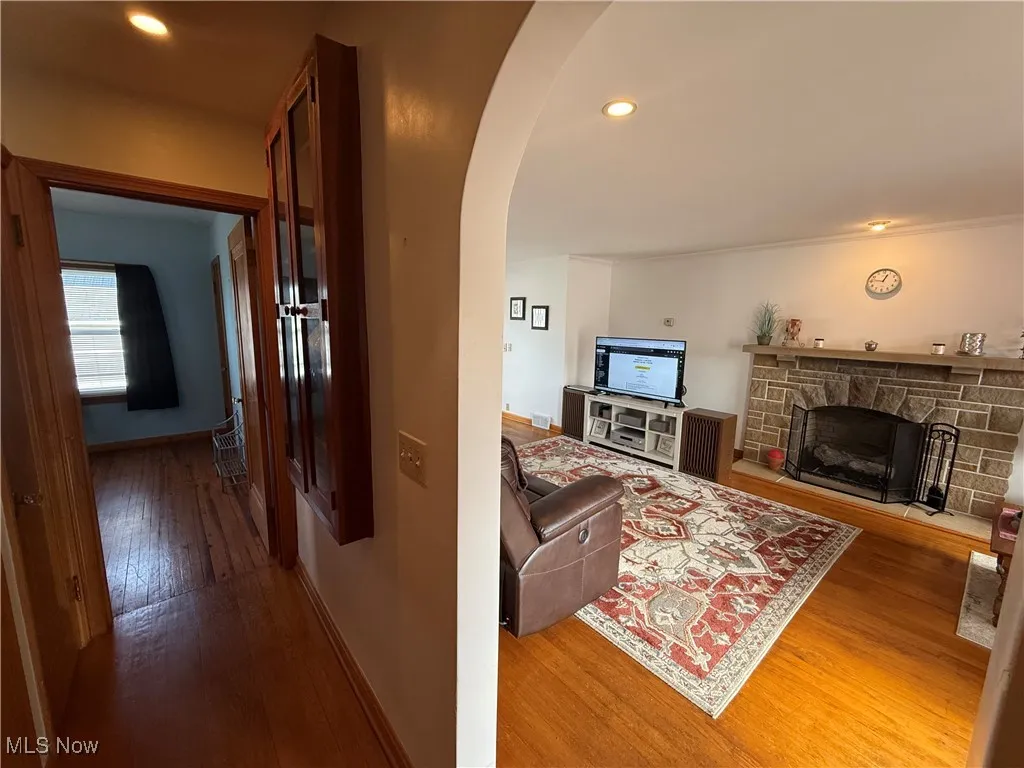 Living room with arched walkways, hardwood / wood-style floors, recessed lighting, and a stone fireplace