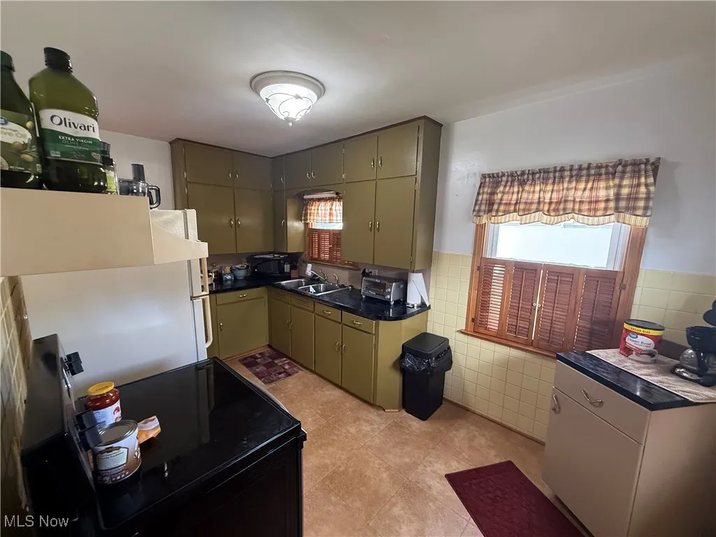 Kitchen with dark countertops, black range with electric stovetop, tile walls, light tile patterned floors, and green cabinetry