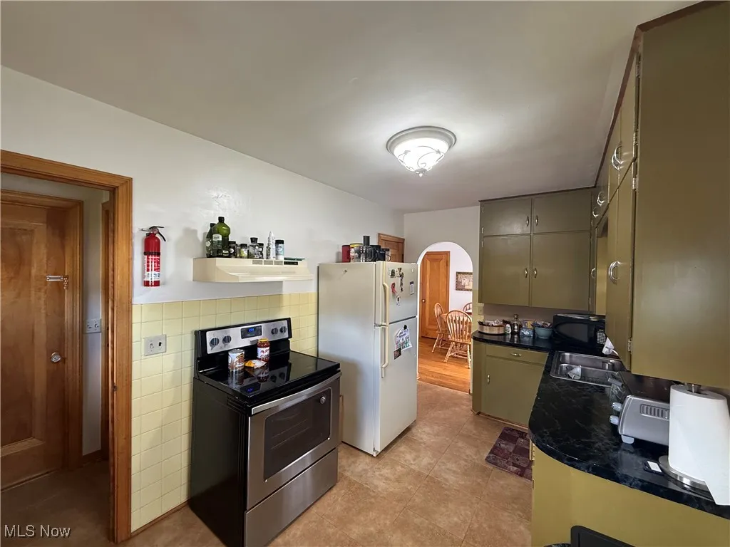 Kitchen with electric range, dark countertops, freestanding refrigerator, arched walkways, and open shelves