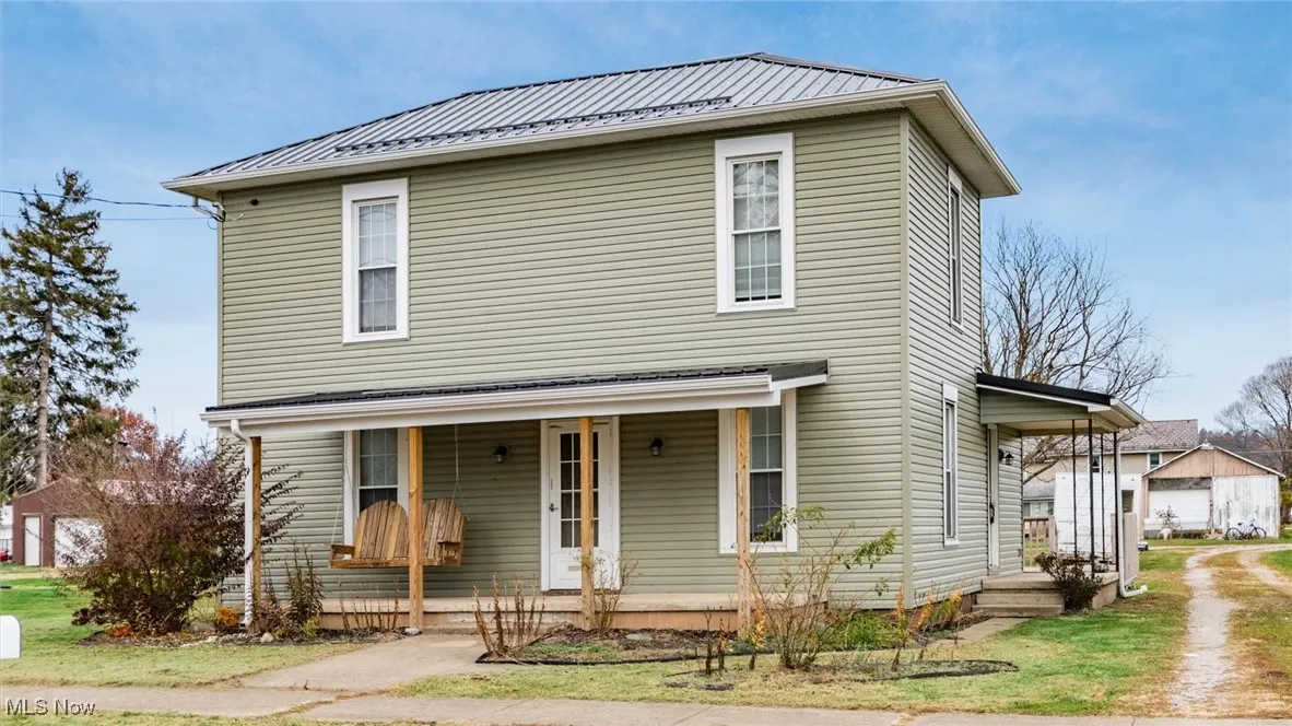 Traditional-style house with a metal roof, covered porch, a garage, and a front lawn