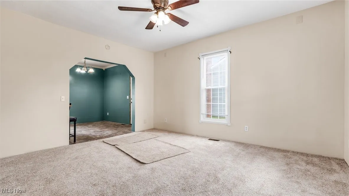 Carpeted empty room featuring arched walkways, a ceiling fan, and a chandelier