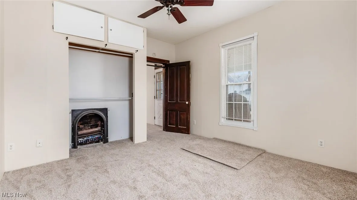 Unfurnished living room with light carpet, ceiling fan, and a fireplace