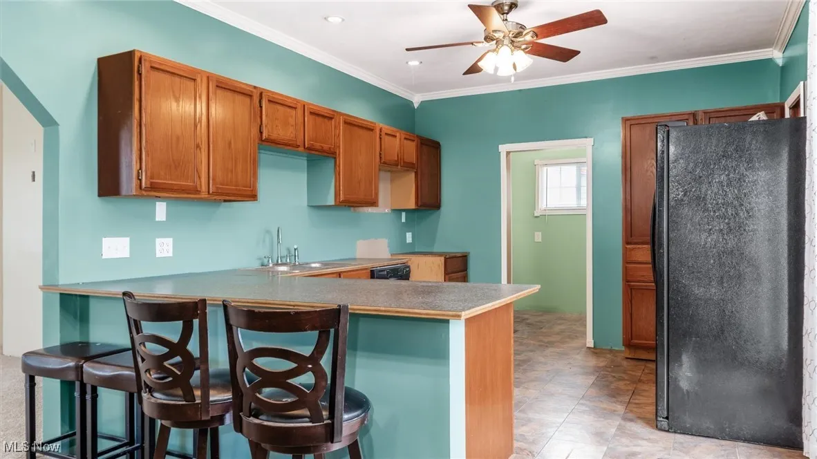 Kitchen with freestanding refrigerator, a breakfast bar, ornamental molding, brown cabinetry, and a peninsula