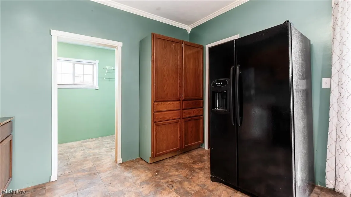 Kitchen with black fridge, brown cabinetry, ornamental molding, and stone finish floors