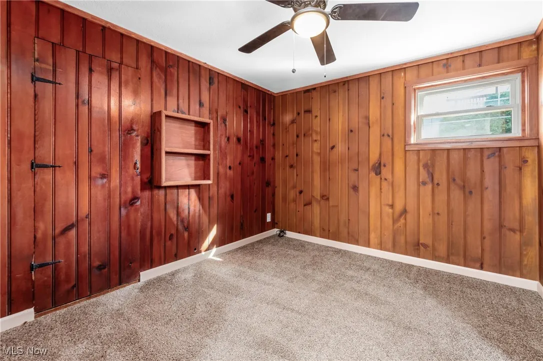 Carpeted spare room featuring wooden walls and baseboards