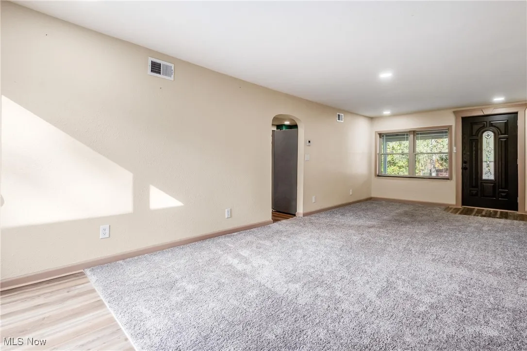 Unfurnished living room featuring arched walkways, recessed lighting, wood finished floors, and carpet
