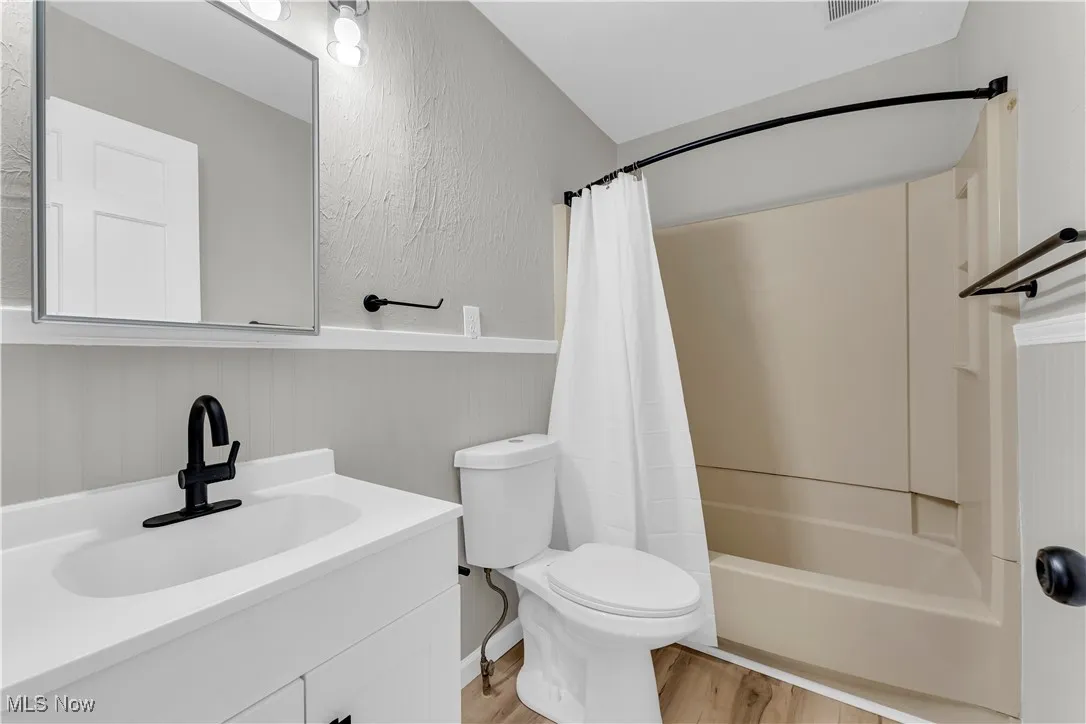 Bathroom with vanity, shower / tub combo with curtain, light wood-style flooring, wainscoting, and a textured wall