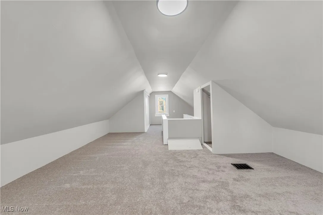 Bonus room with lofted ceiling and light colored carpet