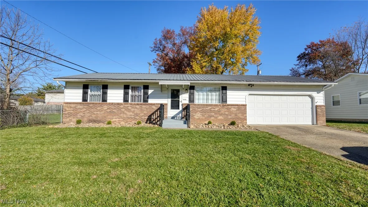 Ranch-style house with brick siding, driveway, a front lawn, an attached garage, and a metal roof