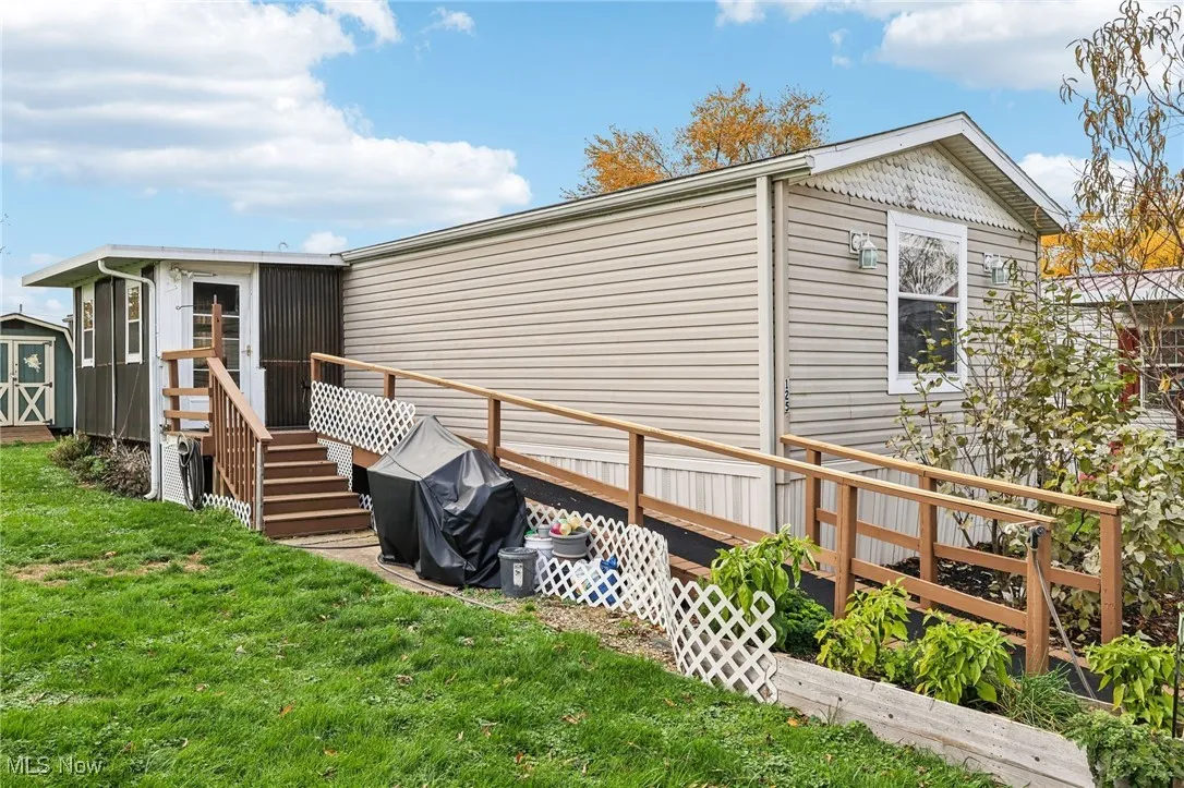 View of side of home with a wooden deck, a yard, and a storage unit