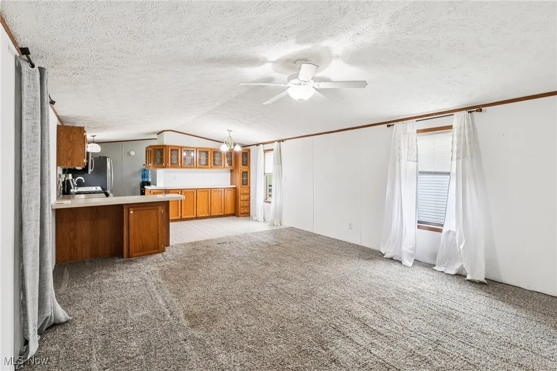 Unfurnished living room featuring light carpet, lofted ceiling, a chandelier, ceiling fan, and a textured ceiling